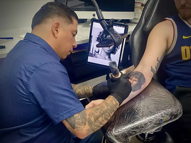 Image: A shot of Artis Garcia tattooing a portrait of Jim Morrison on the inner forearm of a client.