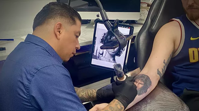 A shot of Artis Garcia tattooing a portrait of Jim Morrison on the inner forearm of a client.