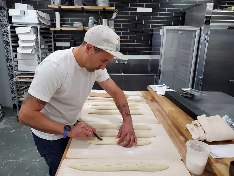 Image: a man scores bread dough in a kitchen