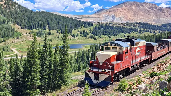 The Leadville Railroad train backdropped by evergreen trees and a rocky peak