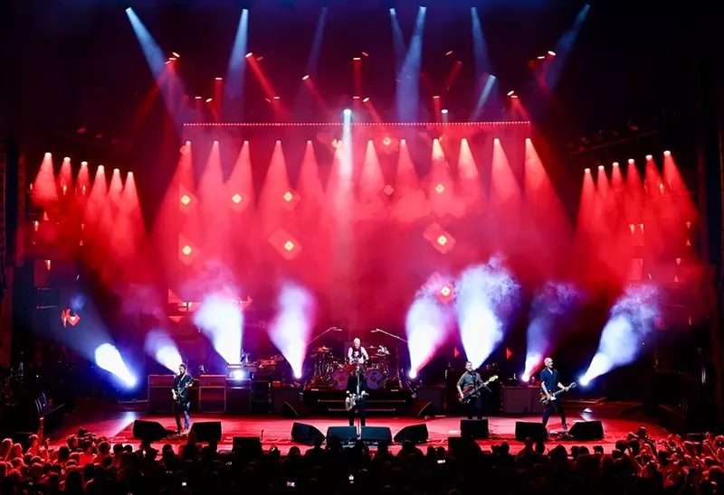 Image: band on stage with red lights in the background