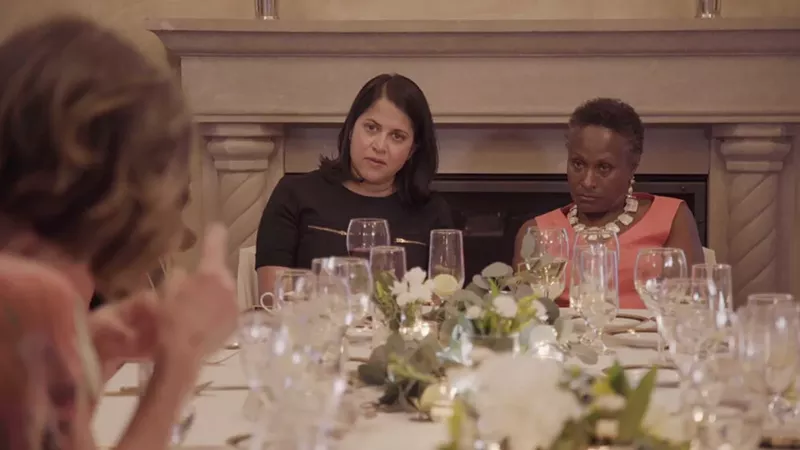 Image: Women sit at a fancy table covered in wine glasses and white flowers.