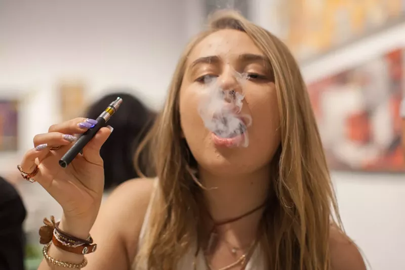 Image: Young woman blows smoke while vaping.