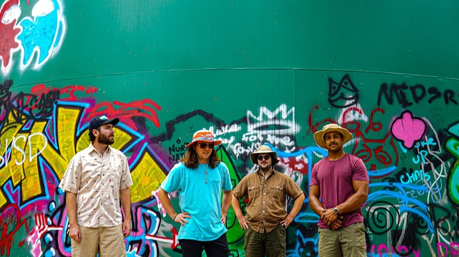 bandmates pose against a green wall with graffiti