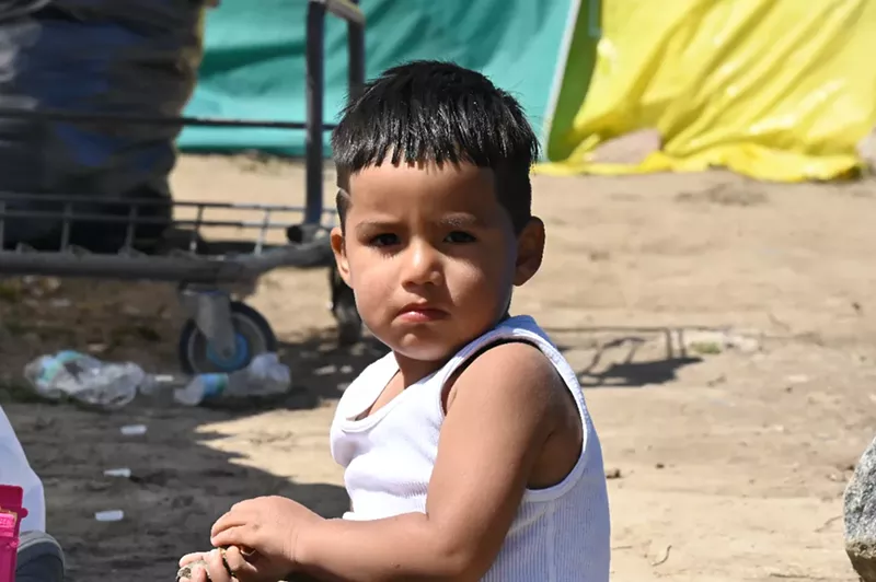 Image: A kid sits in an encampment.