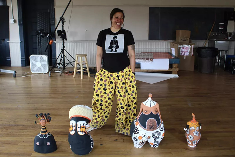 Image: A woman stands with clay figurines