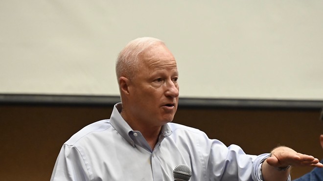 Aurora Mayor Mike Coffman speaks with a microphone in his hand at a town hall.