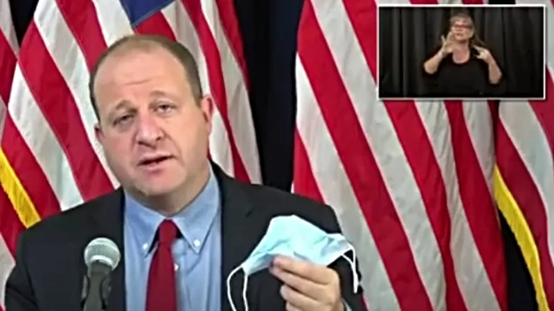 Image: Governor Jared Polis holding a mask at a press conference earlier this month.