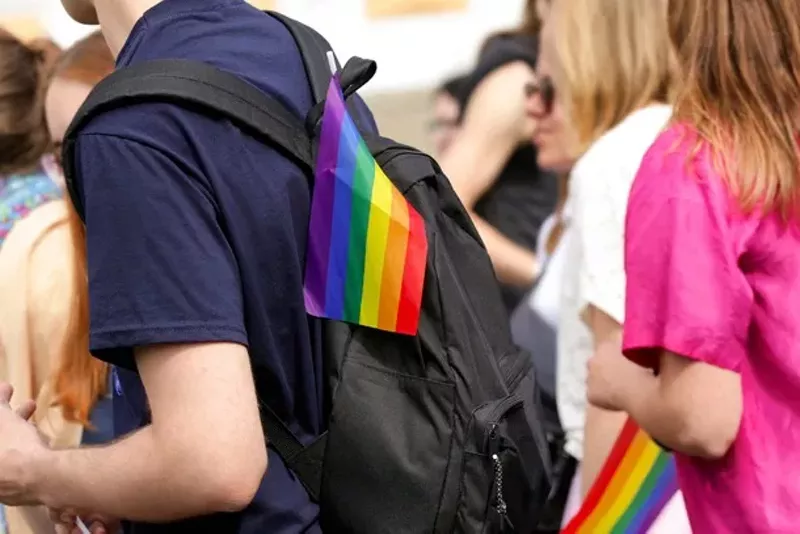 Image: A student wearing a backpack with a small rainbow flag on it, symbolizing LGBTQ pride.