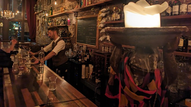 man in a vest standing behind a bar