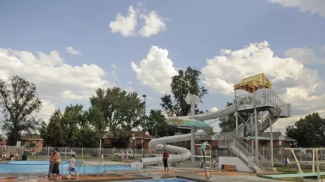 A white water slide winds its way into a blue, rectangular pool.