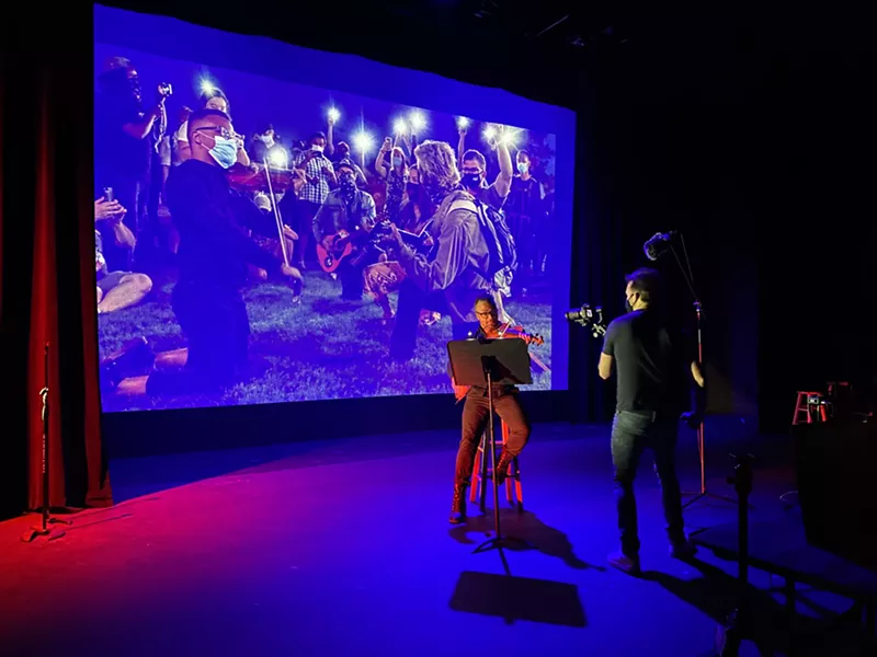 Image: Jukka Pawley plays violin in front of a photo of the violin vigil he led for Elijah McClain in the summer of 2020, taken by John Moore.