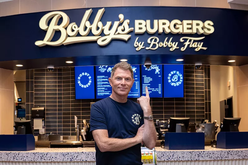 Image: a man stands in front of a sign inside a restaurant