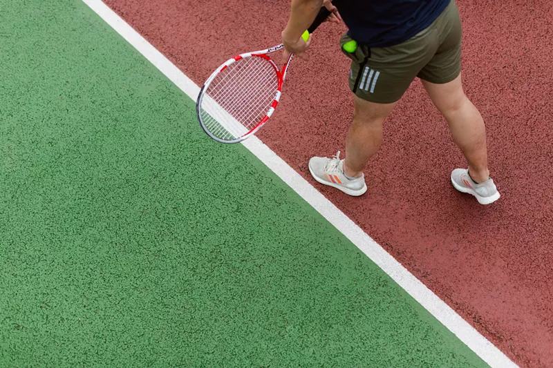 Image: A tennis player holding a racket and a tennis ball prepares to serve.
