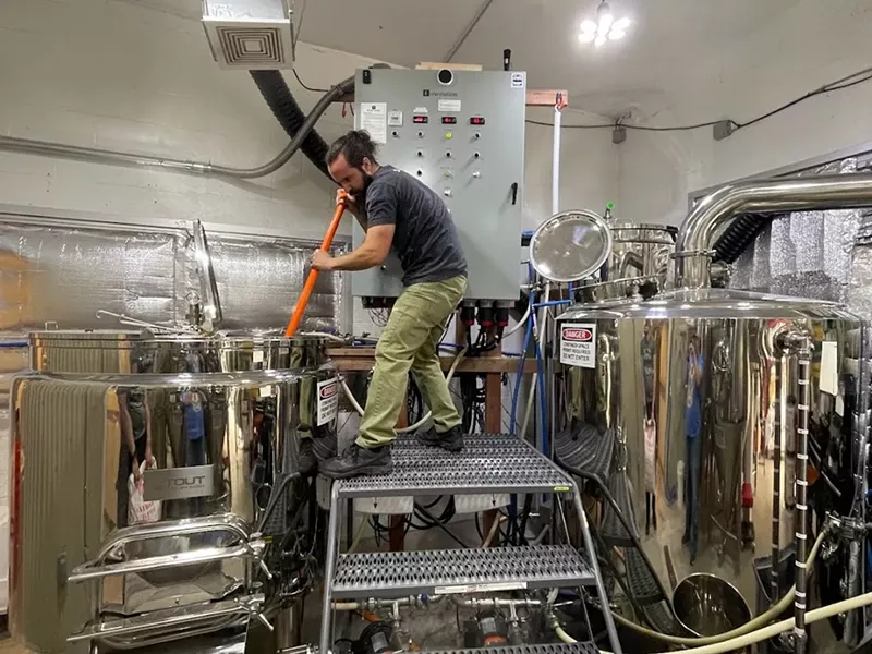 Image: a man stirring a large metal vat