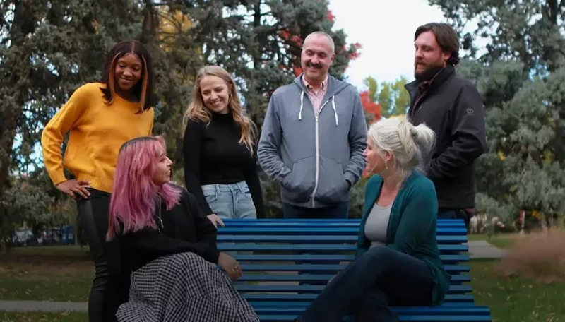 Image: group of people gathered around a blue bench