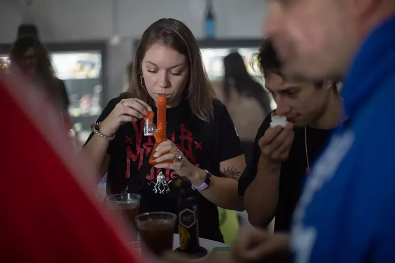 Image: A woman hits weed from a bong as a man smells rosin