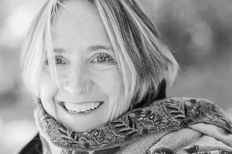 Image: a black and white photo of a smiling blonde woman wearing a scarf