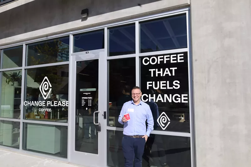 Image: man standing in front of a window that says "coffee that fuels change"