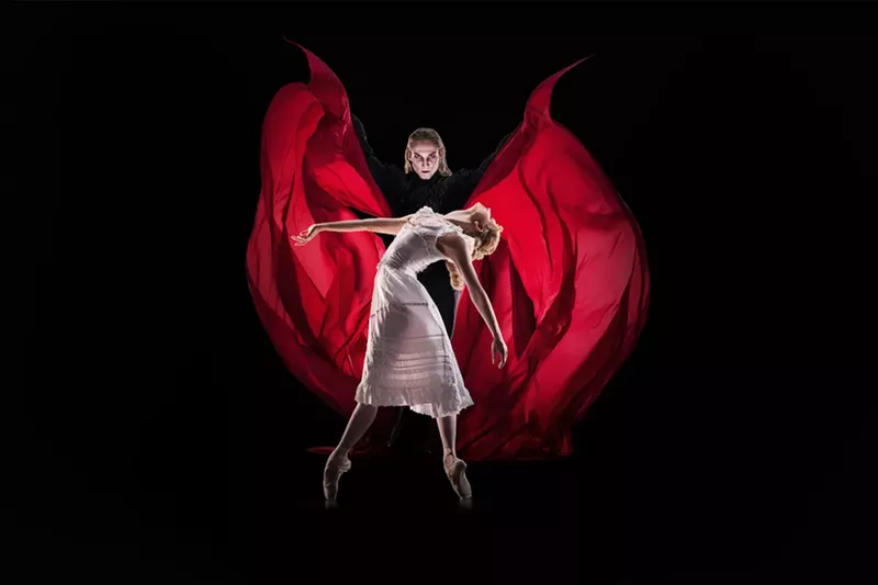 Image: A man wearing a red cape stands behind a woman.