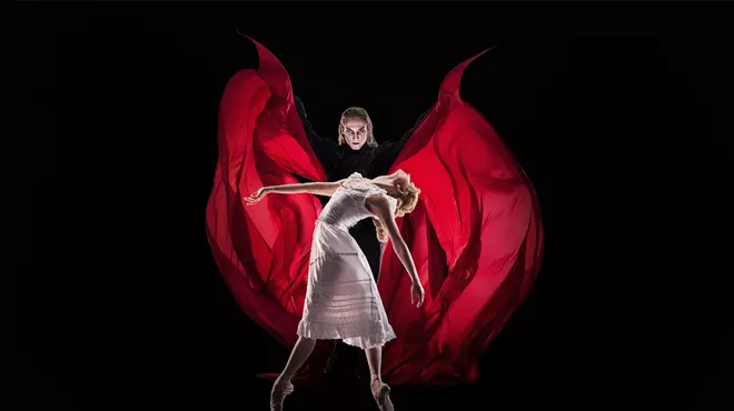 A man wearing a red cape stands behind a woman.