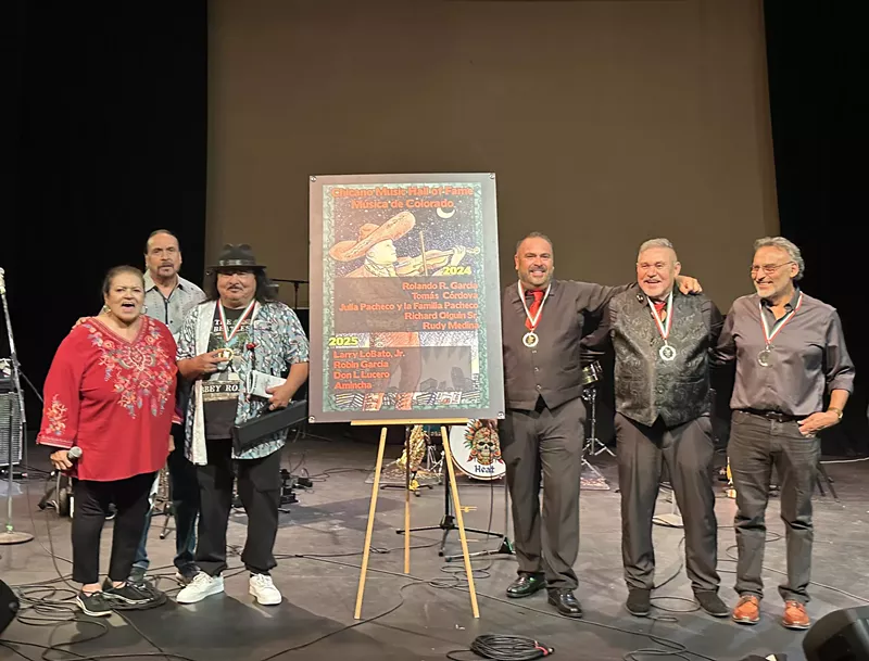 Image: The four inductees of the Chicano Music Hall of Fame stand before a crowd on stage at Su Teatro Cultural & Performing Arts Center.