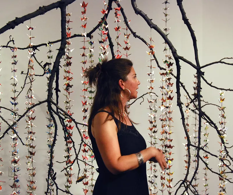 Image: Angela Beloian with "Phoenix," a sculpture of 1,000 cranes folded from recycled mail-order catalogues. Art League Houston, Texas, 2009.