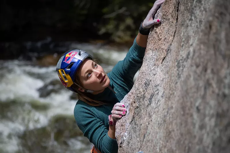 Image: A woman climbs a rock.