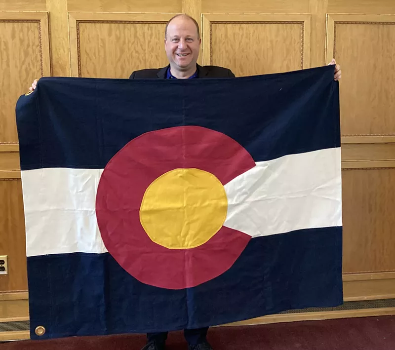 Image: Colorado Governor Jared Polis poses with a Colorado State Flag made of hemp fiber in 2021. The same flag will fly over the State Capitol Building Thursday, June 8.
