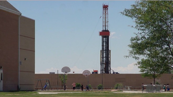 In the foreground, are basketball hoops. In the background, a fracking rig.