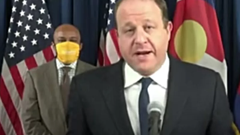 Image: Governor Jared Polis during a November 17 press conference, with a masked Mayor Michael Hancock in the background.