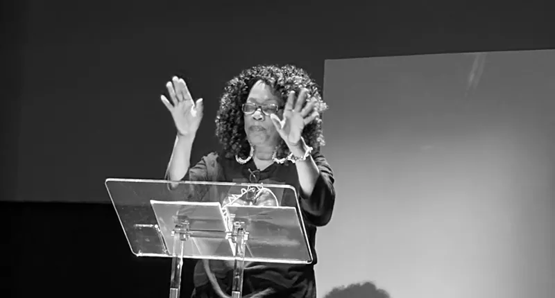 Image: A Black woman stands behind a podium.