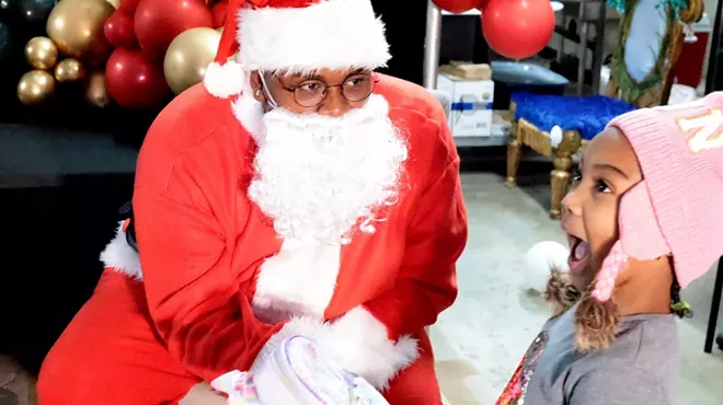 A Black Santa gives presents to a kid.