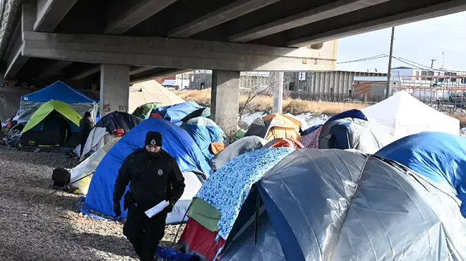 A Denver police officer walks among tents an emptied out migrant encampment.