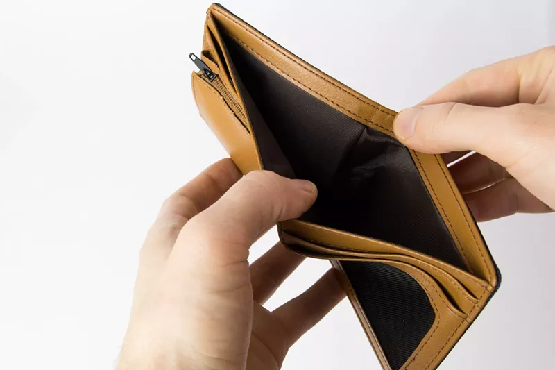 Image: A pair of white hands pry open an empty wallet with their thumbs.