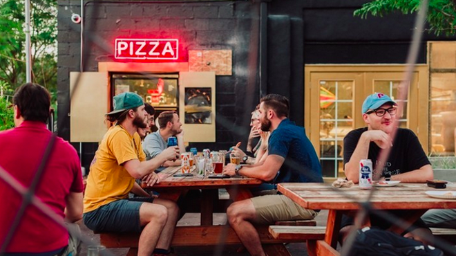 people sitting at picnic tables under a "pizza" sign