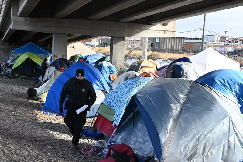 Image: A Denver police officer walks among tents an emptied out migrant encampment.