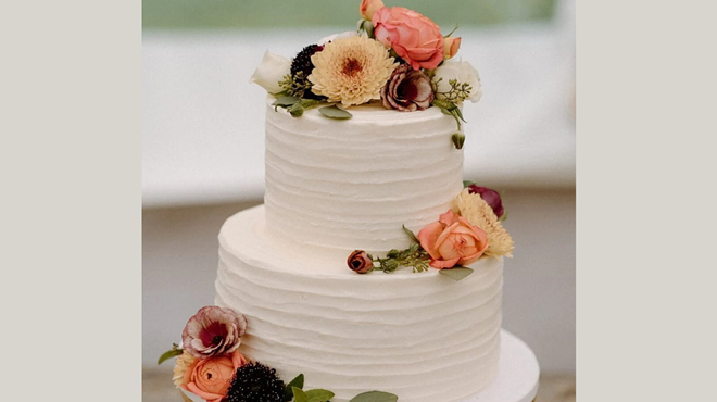 A vegan two-tier wedding cake from The Cake Bar, featuring white frosting and fresh flowers