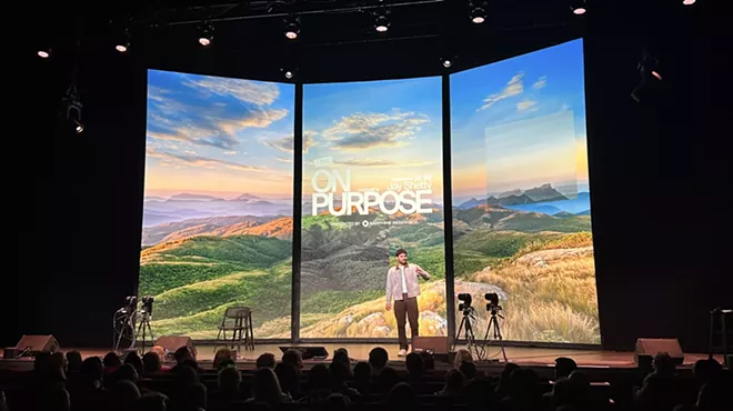 Jay Shetty backdropped by a mountain scene on three digital panels while on stage at the Ellie Caulkins Opera House