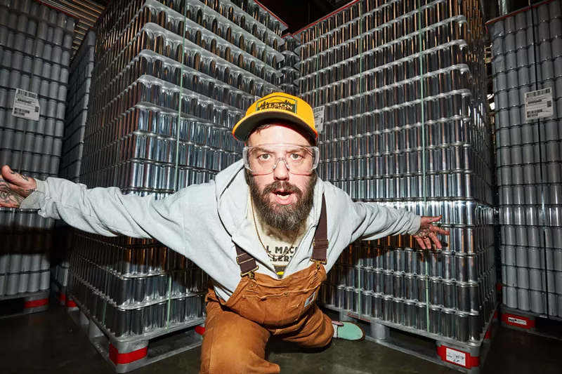 Image: Jordan Childs posed in front of pallets of aluminum beer cans
