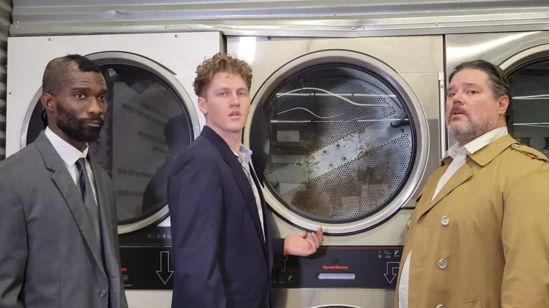 Image: Three men stand in a laundry mat.