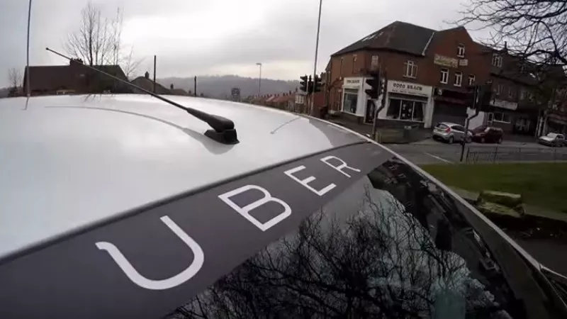 Image: A white car displays the word UBER across the top of its windsheild.