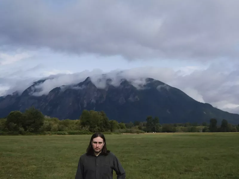 Image: man stands in field in front of mountain