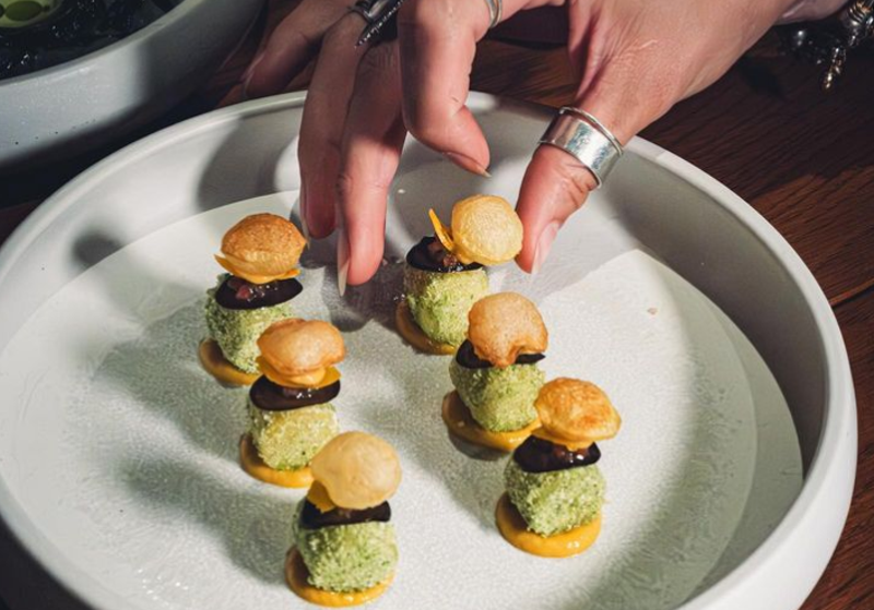 Image: a hand reaching for a small appetizer on a place