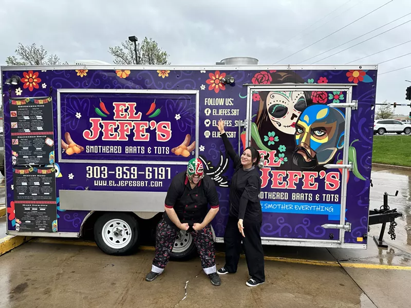 Image: a man in a lucha libre mask and a woman stand in front of a food truck.