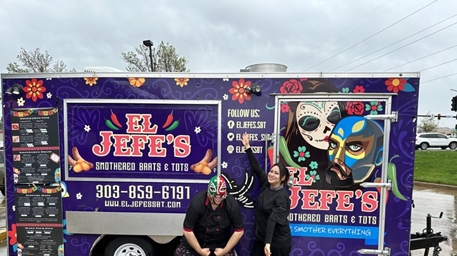a man in a lucha libre mask and a woman stand in front of a food truck.