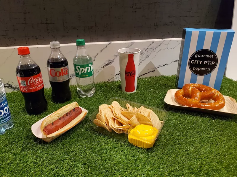 Image: bottles of soda, a hot dog, nachos, a pretzel and a bag of popcorn