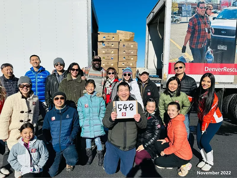 Image: A crowd of people stand in front of two large trucks, with a sign that has "538" written on it.