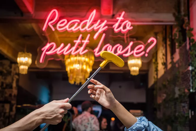 Image: hand reaching for a putter in front of a neon sign