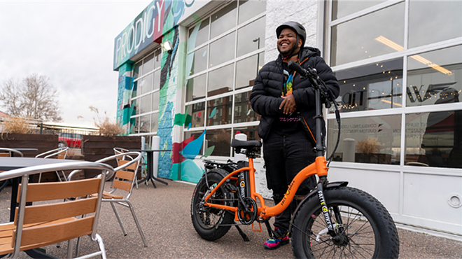 A man stands behind his orange electronic bike.